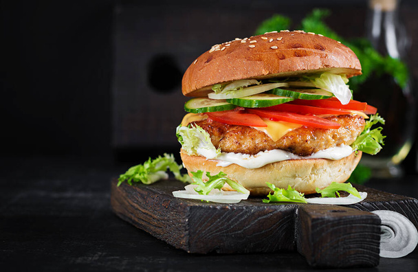 Hamburger with chicken burger meat, cheese, tomato, cucumber and lettuce on wooden background. Tasty burger. Close up - 写真・画像