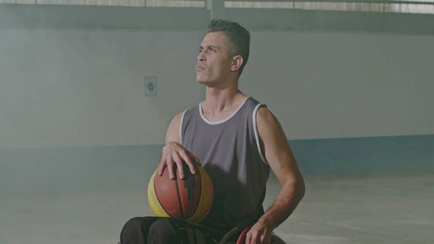 Tekerlekli sandalyede top tutan bir İspanyol engelli basketbolcu. Engelli ve belden aşağısı felçli bir sporcunun portresi. Spor ve kararlılık kavramı - Fotoğraf, Görsel