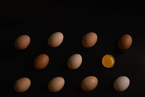 Eggs of different shades on a black background and one more broken  - Photo, Image