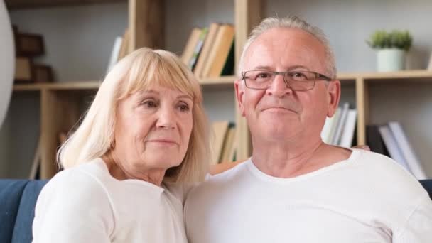 Ritratto ravvicinato di una coppia in pensione che si abbraccia seduta sul divano in salotto. Coppia felice di nonni - Filmati, video
