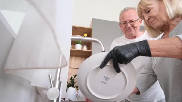 Gri saçlı büyükbaba ve büyükanne mutfakta bulaşık yıkıyorlar. Mutlu emekliler mutfakta birlikte vakit geçirirler. - Video, Çekim