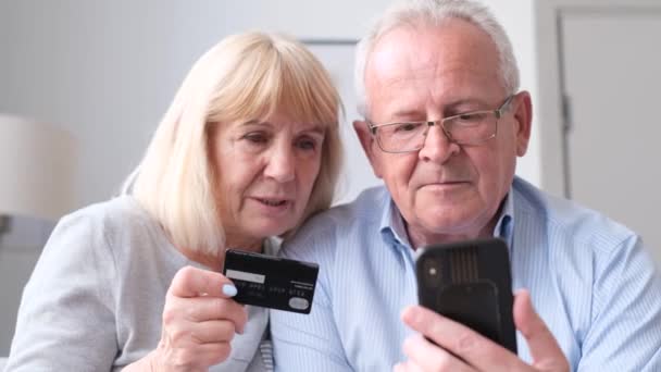 Ένα ζευγάρι συνταξιούχων ψωνίζει online χρησιμοποιώντας ένα smartphone. Άχρηστος διακανονισμός με τραπεζική κάρτα. Βίντεο 4k - Πλάνα, βίντεο