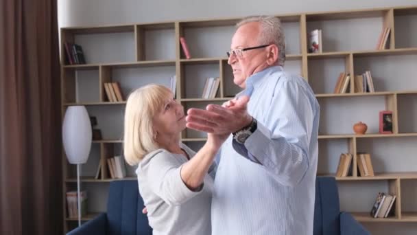 Gelukkig actief seniorenpaar dansend samen thuis, vrolijke zorgeloze oude man en vrouw dansend op muziek, genietend van het weekend of jubileum vierend in de woonkamer - Video