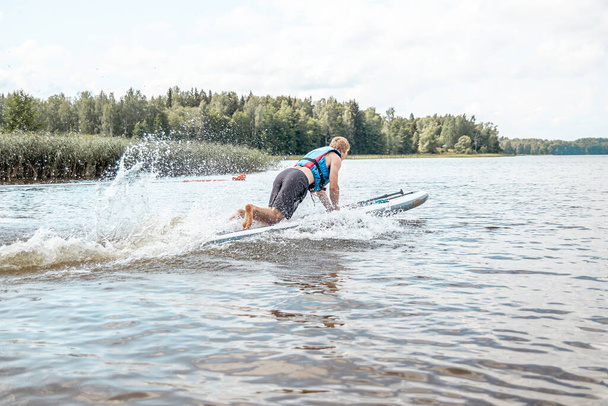 Remar en una tabla de SUP en un lago en un día soleado. Stand up paddle boarding - impresionante recreación activa al aire libre. - Foto, Imagen