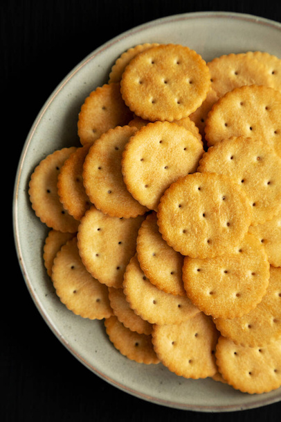 Salty Round Crackers on a Plate on a black surface, top view. Flat lay, overhead, from above.  - Fotografie, Obrázek