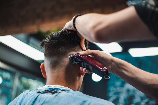 Tiro de perto de um homem a cortar o cabelo na barbearia. Cabeleireiro masculino servindo cliente, fazendo corte de cabelo usando máquina e pente
. - Foto, Imagem