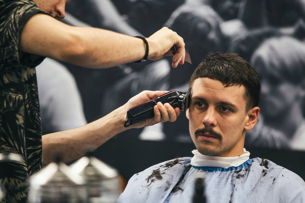 Close up shot of man getting trendy haircut at barber shop. Male hairstylist serving client, making haircut using machine and comb. - Photo, Image