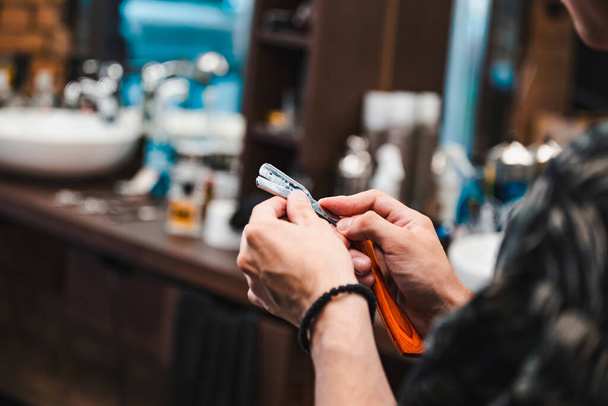 Master disinfecting shaving instrument before use. Young man spray changing razor, free space. Occupation, beauty, barbershop, grooming, safety concept - 写真・画像