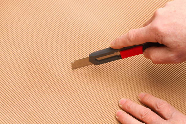 Man cutting a corrugated cardboard with a black cutter - Valokuva, kuva