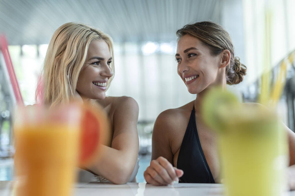Fiatal nők koktélt isznak a medence bárjában. Idilli nyaralás koncepció. - Fotó, kép