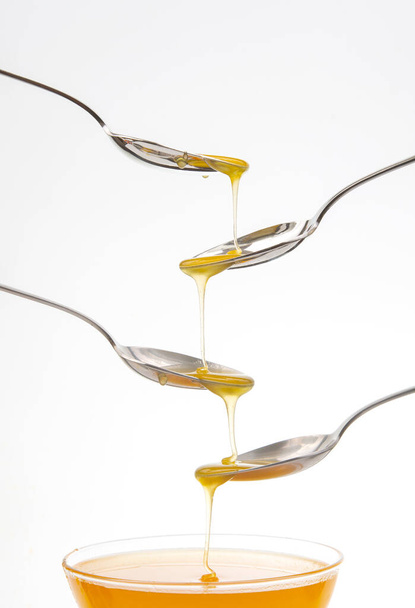 Fresh floral honey drips from a spoon into a spoon on a white background. Organic vitamin food. - Foto, Bild