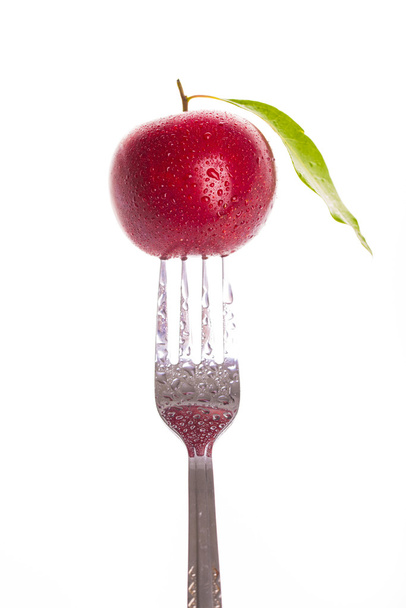 Red plum pricked on the steel fork isolated - Fotoğraf, Görsel