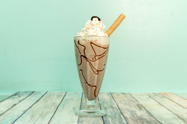 Delicious chocolate milkshake with syrup, whipped cream, chopped chocolate chip cookies and cookie straw in a glass jar - Foto, Bild