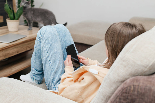 Sosiaalinen media. Koulutyttö istuu sohvalla puhelin käsissään ja chatit tai kommunikoi ystävien kanssa. Lapset ja vempaimet. Nuori bloggaaja - Valokuva, kuva