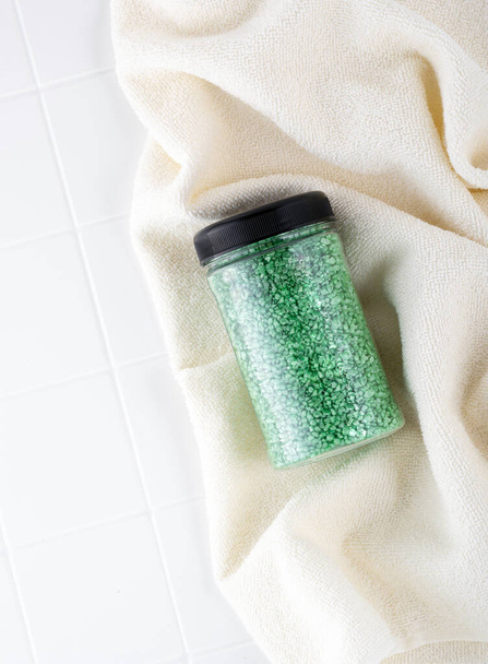 Pacote de sal de cristal glitter verde em uma toalha de banho bege. Frasco de sal marinho verde cintilante para spa em casa. Ideia de relaxamento, aromaterapia e autocuidado. O efeito da água do mar no cabelo. - Foto, Imagem