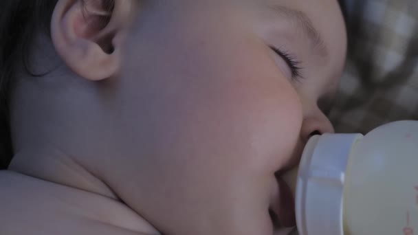 Portrait of a sleeping little child with a bottle in his mouth. The baby eats in a dream. The baby drinks milk from a bottle and sleeps. High quality 4k footage - Felvétel, videó