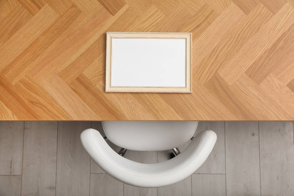Empty photo frame on wooden table near chair indoors, top view - Photo, image