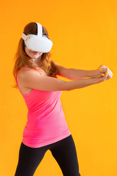 Νεαρή γυναίκα που χρησιμοποιεί ακουστικά εικονικής πραγματικότητας. Απομονωμένα σε πορτοκαλί φόντο. - Φωτογραφία, εικόνα