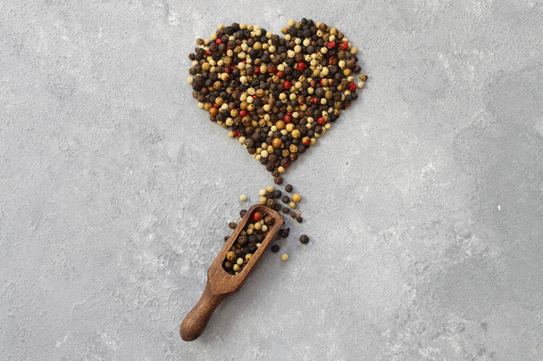 Mixture of peppercorns in heart shape isolated on white background. With wooden scoop. - Foto, afbeelding