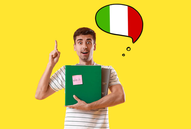 Young man with folders and raised index finger on yellow background. Studying of Italian language - Photo, Image