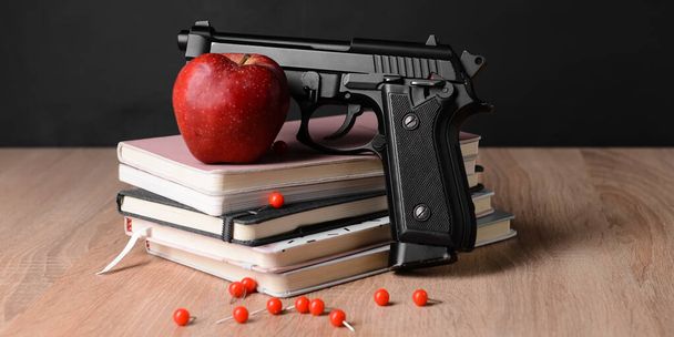 Пистолет, яблоко и книги на столе в классе. Концепция стрельбы в школе - Фото, изображение