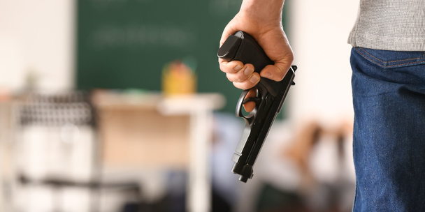 Een mannelijke terrorist met een pistool in de klas. Schietpartij op school - Foto, afbeelding