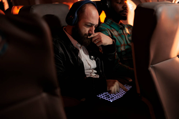 Young entrepreneur working on laptop and flying on business trip with airplane in economy class. International commercial flight with airline service, using computer during sunset. - Photo, Image