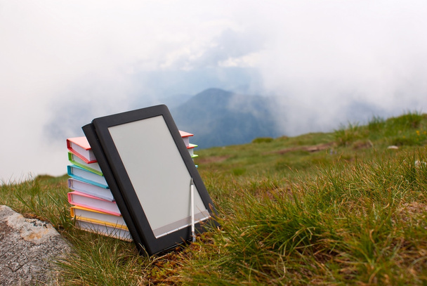 stos kolorowych książek i czytnik książek elektronicznych na trawie - Zdjęcie, obraz