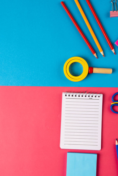 Vertical composition of colorful school equipment with notebook on blue and pink surface. School equipment, tools, learning and creativity concept. - Фото, зображення