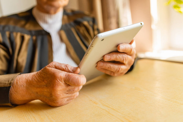 Старшая женщина делает видеозвонок с планшетного компьютера дома возле стола. - Фото, изображение