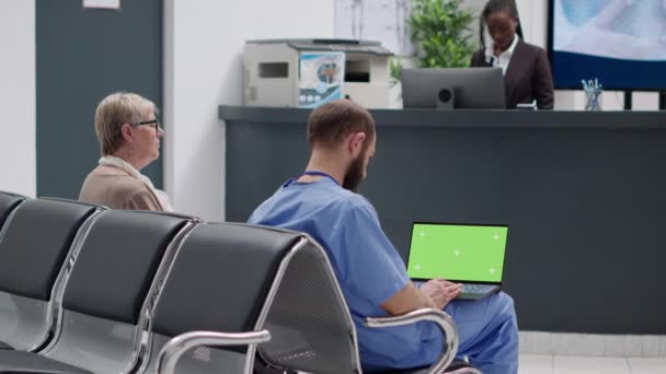 Mužská sestra analyzující zelenou obrazovku na notebooku v čekárně, sedící v nemocničním přijímacím prostoru. Prázdná šablona copyspce s maketovým pozadím a izolovaným klíčem chroma. Trojnožka. - Záběry, video