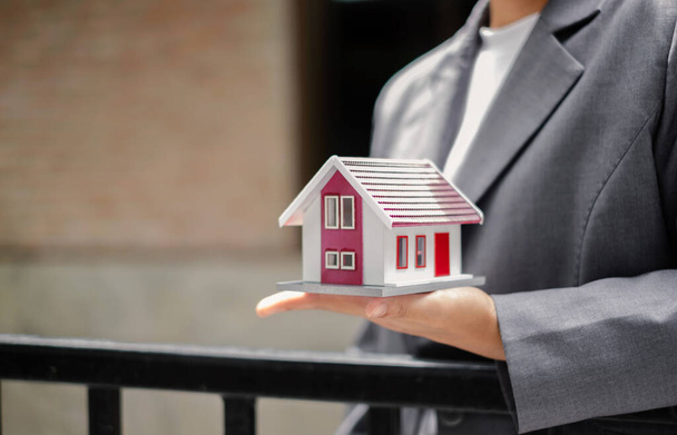 Home insurance concept and real estate. Businesswoman holding a house model working in investment about renting a house, buying a house, and home insurance. - 写真・画像