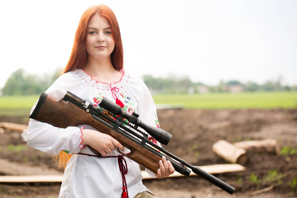 Uma menina em um vestido nacional ucraniano bordado com uma arma em suas mãos, um símbolo da Ucrânia defendendo-se contra a invasão russa - Foto, Imagem
