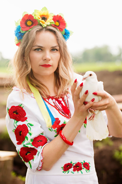 A beautiful Ukrainian woman in Ukrainian national embroidered dress with a white dove in her hands, a symbol of peace in Ukraine - Valokuva, kuva