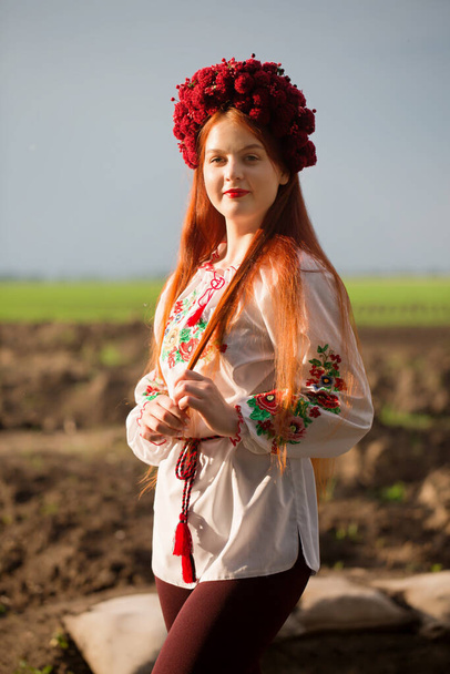 Unbreakable Ukraine. Portrait of a red-haired Ukrainian woman in an embroidered shirt and a wreath against the background of trenches - Foto, afbeelding