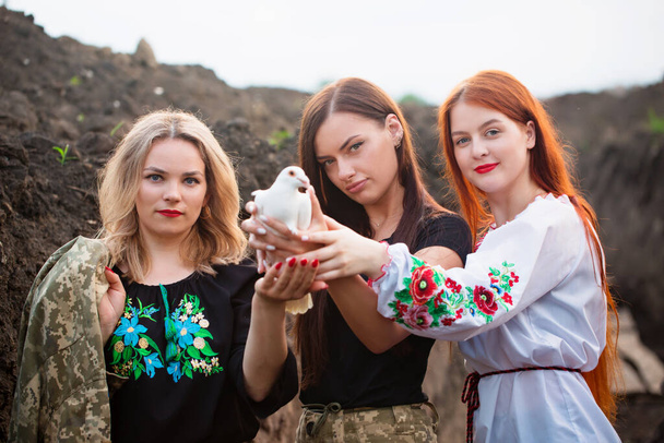 Drie verschillende Oekraïense vrouwelijke verdedigers houden een duif van vrede, een symbool van vrede in Oekraïne - Foto, afbeelding