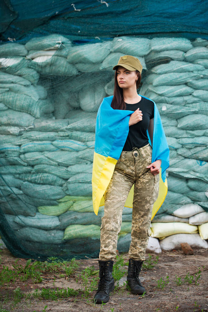 Ουκρανικό κορίτσι με τη στολή των ενόπλων δυνάμεων της Ουκρανίας κοντά στο σημείο ελέγχου με τη σημαία της Ουκρανίας - Φωτογραφία, εικόνα