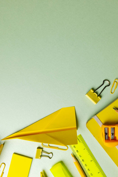 Vertical composition of yellow school equipment with paper plane on green surface with copy space. School equipment, tools and creativity concept. - Photo, image
