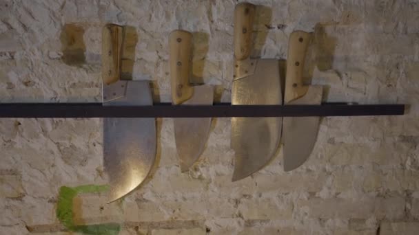 Push-out of large knives hanging by light brick wall in restaurant - 4K Horizontal video - Filmati, video