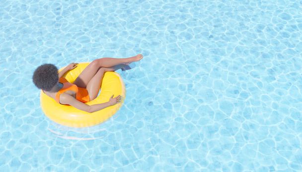 3D illustration of black female tourist in swimwear with Afro hairstyle relaxing in yellow tube in clean water of swimming pool during summer vacation - Foto, Imagen