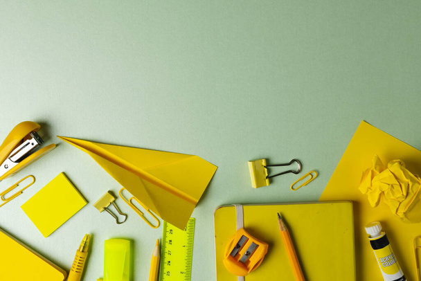 Composition of yellow school equipment with paper plane on light green surface with copy space. School equipment, tools and creativity concept. - Photo, Image