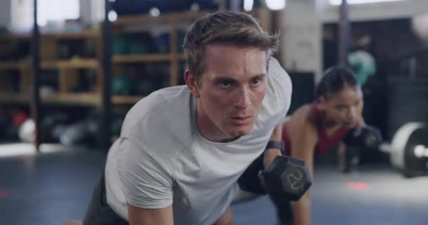 Trainer lifting dumbbell weights in plank position and leading a fitness HIIT gym class. Two focused, fit, active and athletic people exercise training in workout for core strength and tricep muscles. - Video