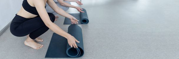 Close-up of an attractive young woman laying out a blue yoga or fitness mat before exercising in the studio. Healthy lifestyle.  - Фото, изображение