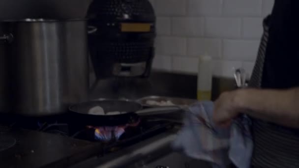 Handheld side view of chef flambeing food in restaurant kitchen - 4K Horizontal video - 映像、動画