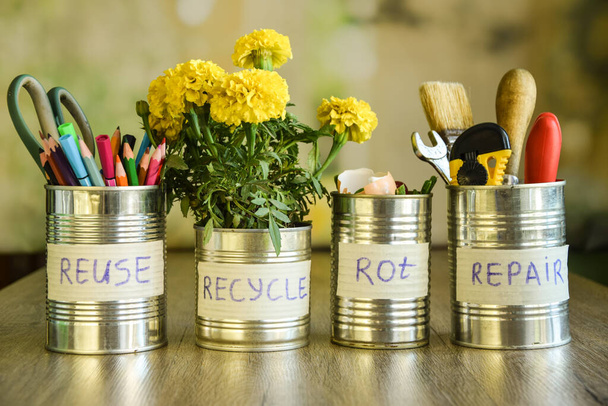 Using cans on different purposes at domestic life. Stationery, home flower, tools, organic waste in tin cans standing in row on blurred background. Upcycling, Environment conservation. Reducing waste - 写真・画像