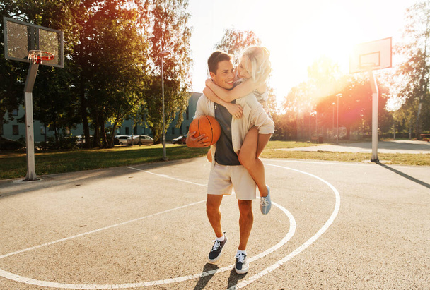 summer holidays, love and people concept - happy young couple with ball having fun on basketball playground - Фото, изображение