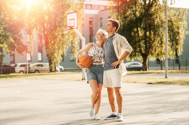 sport, love and people concept - happy young couple with ball hugging on basketball playground - Foto, Imagem