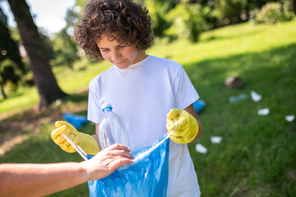 Garbage. Someone helping a curly-haired teen to gather garbage - Фото, изображение