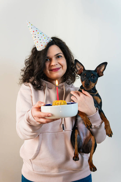 Chica joven feliz dando pastel casero a su perro, en el interior. Concepto de libre de niños por elección y celebración de la fiesta de cumpleaños del perro - Foto, imagen