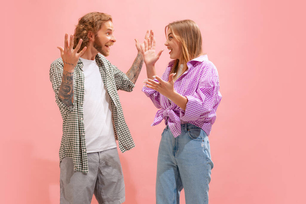 Portrait of young man and woman in casual clothes actively communicating, celebrating isolated over pink studio background. Concept of youth, lifestyle, relationship, emotions, facial expression, ad - Fotografie, Obrázek